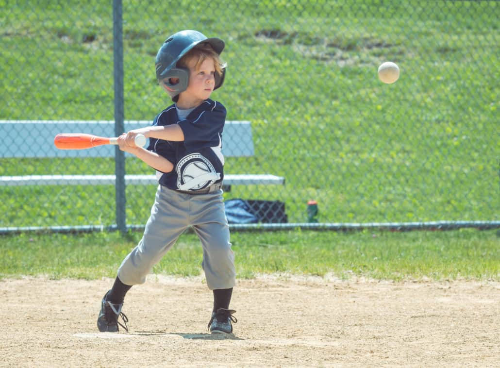 A little boy swings at an incoming baseball.